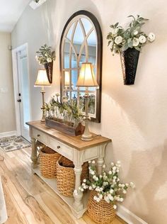 an entryway with flowers and baskets on the floor next to a mirror that is hung above it