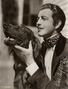 a black and white photo of a man in a suit holding a dog with his mouth open