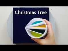 a person holding a christmas tree ornament in front of a blue box with the words christmas tree on it