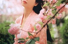 a woman in a pink dress standing next to a tree with flowers on it's branches