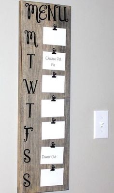 a wooden sign hanging on the side of a white wall with writing and magnets attached to it