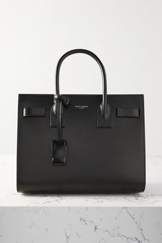 SAINT LAURENT's understated 'Sac De Jour' tote has a structured shape that will fit a book and your makeup bag. Crafted in Italy from black embossed-leather, it has a gold-tone padlock engraved with the brand's moniker and a zipped compartment for your smaller possessions. Use it every day or as a carry-on when travelling. Classic Designer Handbags, Designer Work Bag, Office Bags For Women, Black Designer Bags, Power Outfit, Ysl Tote Bag, Branded Tote Bags, Structured Handbags, Luxury Tote Bags