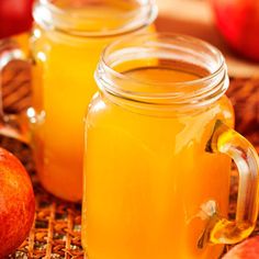 two mason jars filled with apple cider sitting on a table next to sliced apples