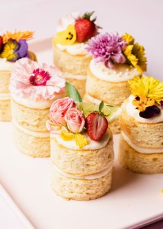 small cakes with flowers and strawberries on top sit on a white plate, ready to be eaten