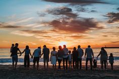 a group of people standing on top of a beach next to the ocean at sunset