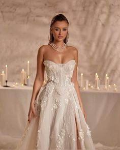 a woman in a wedding dress standing next to candles on a table with white linens