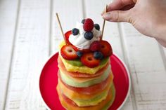 a stack of fruit topped with whipped cream on top of a red plate next to a hand