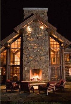 an outdoor fireplace in the middle of a stone building with chairs and tables around it