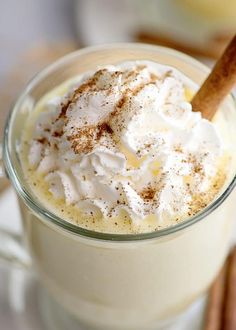 a cup filled with whipped cream on top of a white table next to cinnamon sticks