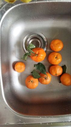 several oranges in a metal sink with leaves on the top and water running down the drain