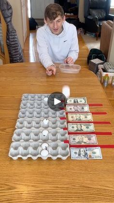 a young man sitting at a table with an egg carton and dollar bills in front of him