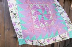 a pink and blue quilt hanging on a wooden fence next to a brown fence with purple flowers