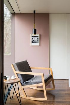 a modern rocking chair in the corner of a room with pink walls and wood flooring