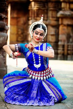 a woman dressed in blue and white is sitting on the ground with her arms outstretched