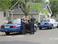 two police officers talking to another officer in the back of a blue car on a residential street