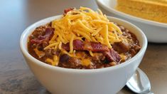 a white bowl filled with chili and cheese on top of a table next to a fork