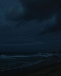 an airplane is flying over the ocean at night with dark clouds in the sky above