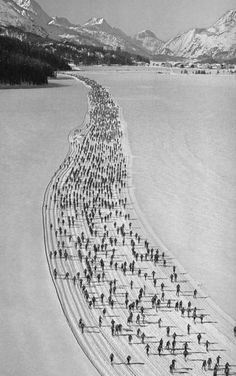 a large group of people skating across a lake in the middle of winter with mountains in the background