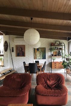 a living room filled with red couches and chairs next to a dining table in front of a white brick wall