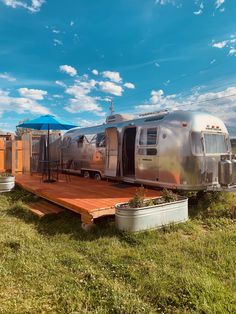 an airstream sits on a wooden platform in the middle of a grassy area under a blue sky with clouds