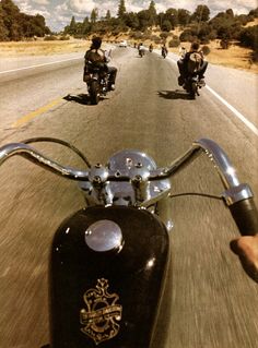 two people riding motorcycles down the road in front of another motorcyclist on a motorcycle