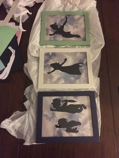 three framed silhouettes sitting on top of a wooden floor next to paper and scissors