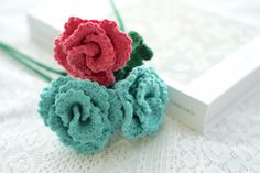 two crocheted flowers sitting on top of a white surface next to a book