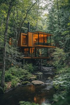 a house in the woods surrounded by trees and rocks, with a stream running through it