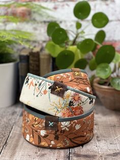 a close up of a flowered belt on a wooden table next to potted plants