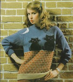 a woman standing in front of a brick wall wearing a sweater with cats on it