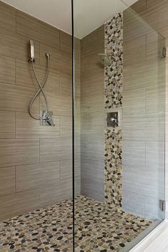 a walk in shower sitting next to a tiled wall and floor covered in pebbles on the outside