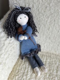 a small doll is sitting on a white blanket and wearing a blue knitted dress