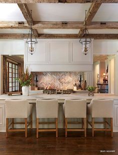 a large kitchen with white cabinets and wooden beams on the ceiling, along with beige upholstered chairs