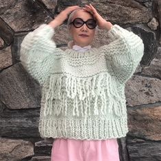 a woman standing in front of a stone wall with her hands on her head and wearing sunglasses