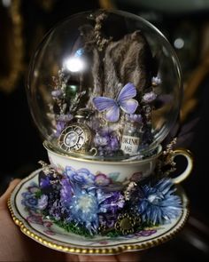 a snow globe with purple flowers and butterflies in it on top of a saucer