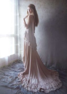 a woman standing in front of a window wearing a long dress with ruffles