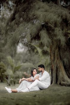 a man and woman sitting under a large tree