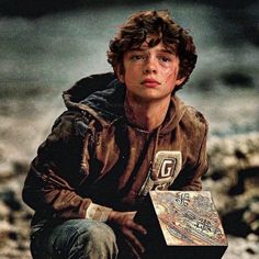 a young boy sitting on the ground with a box in his hand and looking at something