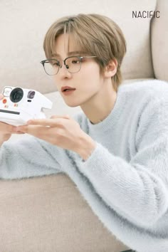 a person sitting on a couch holding a polaroid camera and looking at the camera