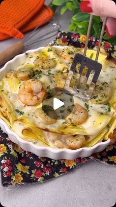 a person is holding a fork over a dish with shrimp and cheese in it on a floral cloth