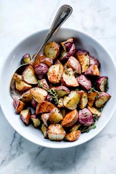 a white bowl filled with roasted potatoes and garnished with herbs