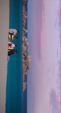 two snowboarders standing on the edge of a cliff looking out at the ocean