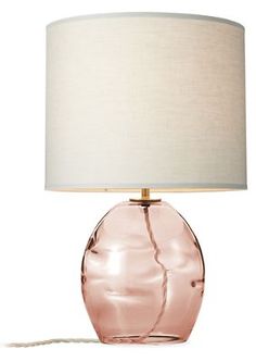 a pink glass table lamp with a white shade on the base and a light bulb plugged in