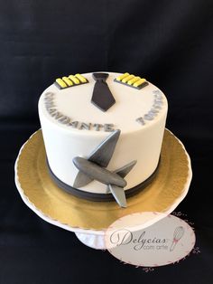 a white cake with an airplane on top is sitting on a gold plate and black background