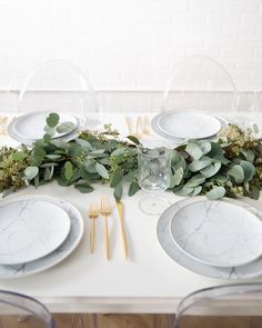 the table is set with white plates and silverware, greenery, and gold utensils