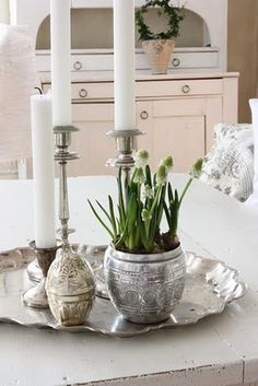 a white table topped with a silver plate covered in flowers and two tall candlesticks