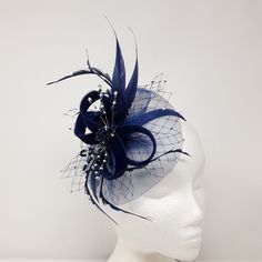 Elegant navy blue velvet and crinoline fascinator with beautiful bead detail. Dainty, lightweight easy to wear trimmed with velvet ribbon , zig zag cut feathers, a cluster and wired sprays of shimmering glass beads and rhinestones at the  centre. finished rhinestone studded navy blue veiling Comes with all three attachments i.e a 5cm crocodile clip, 7cm comb and 1cm wide ribbon covered Alice band to allow you choose which one works best for you.  This design can be made in other colours or a combination of shades to suit. If you would like an extra colour added, please ask we have a vast range of feathers in stock and can usually accommodate.  Measures around 18 cm at the widest point. Blue Curved Brim Evening Fascinator, Elegant Blue Headpiece With Feather Trim, Crinoline Fascinator, Elegant Blue Headband Fascinator, Navy Feather Fascinator, Adjustable Blue Feathered Headpiece, Blue Veil, Alice Band, Rhinestone Studs