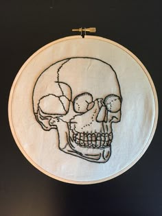 a cross stitched skull is shown on a white hoop hanging from a black wall