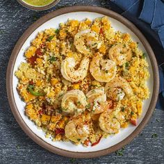 a white plate topped with shrimp and rice next to a bowl of green sauce on a wooden table