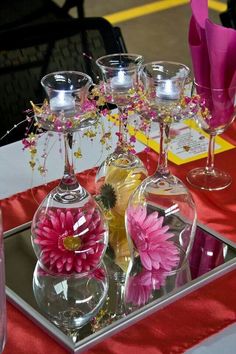 there are many wine glasses on the table with pink flowers in them and one is empty